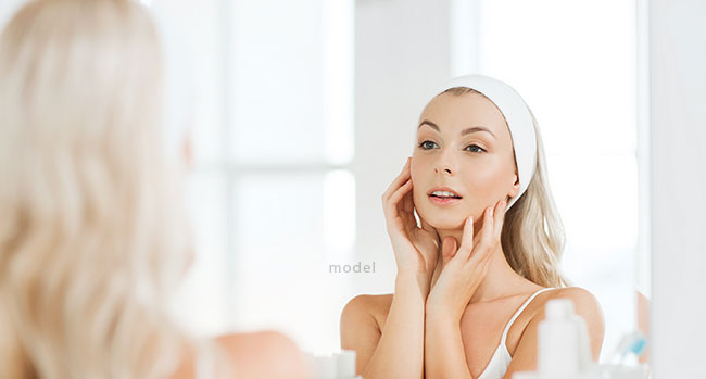 Woman wearing a white headband touching her face while looking in the mirror.